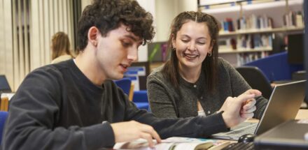 College lecturer and learner looking at book in library