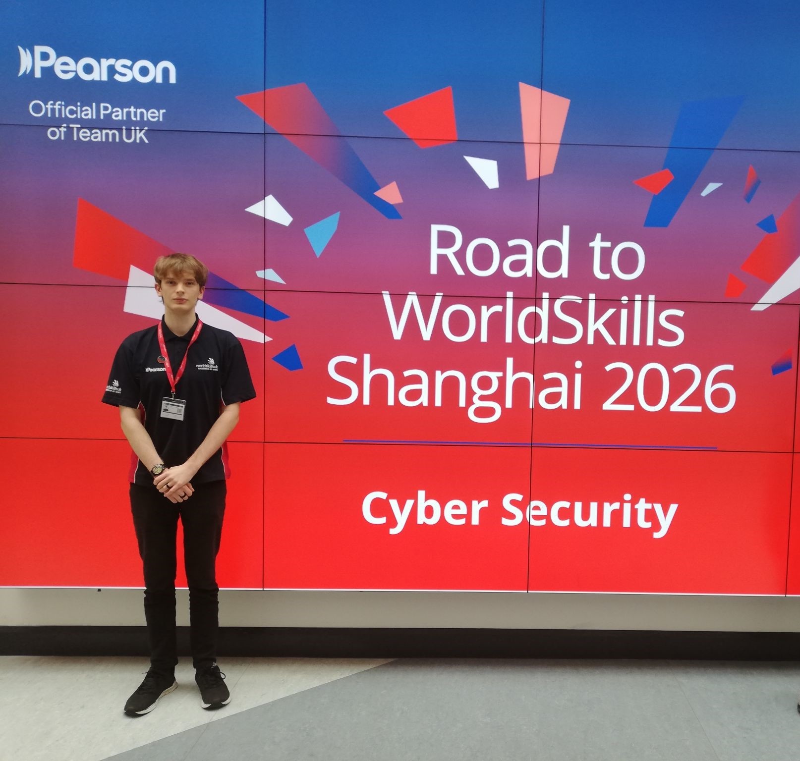 Charlie standing next to a sign which reads 'Road to WorldSkills Shanghai 2026'