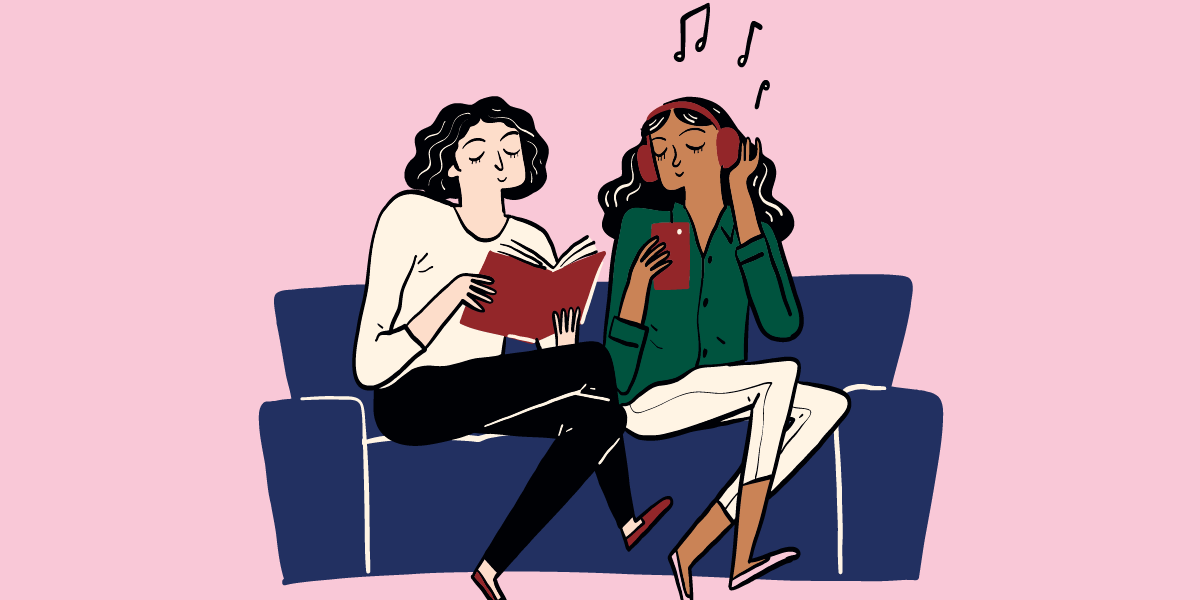Two young people sitting on a sofa. One is reading a book and the other is listening to music.